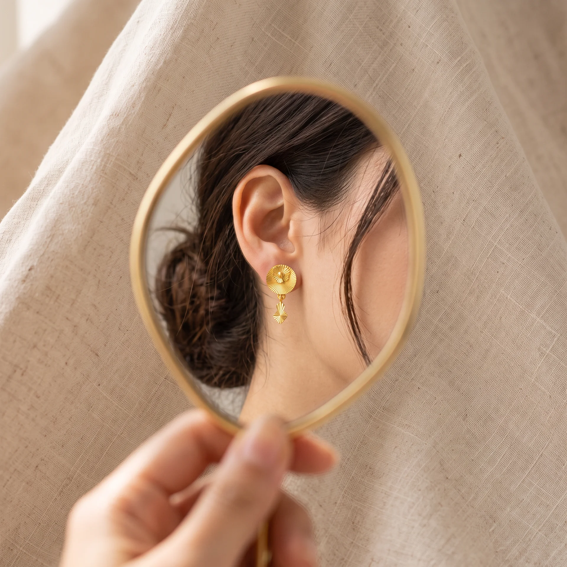 Gold drop earring reflected in a handheld mirror