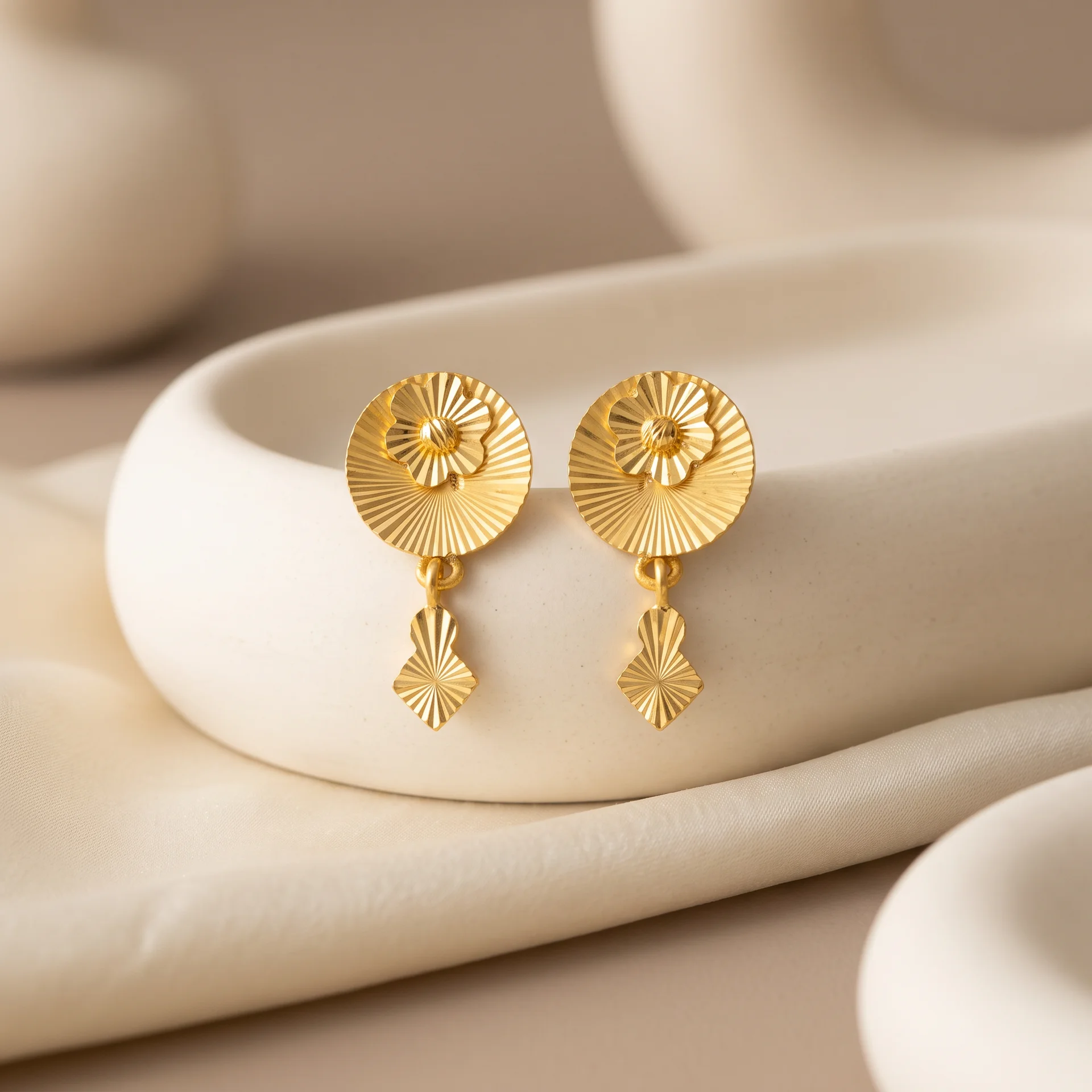 Gold fluted drop earrings on a ceramic dish
