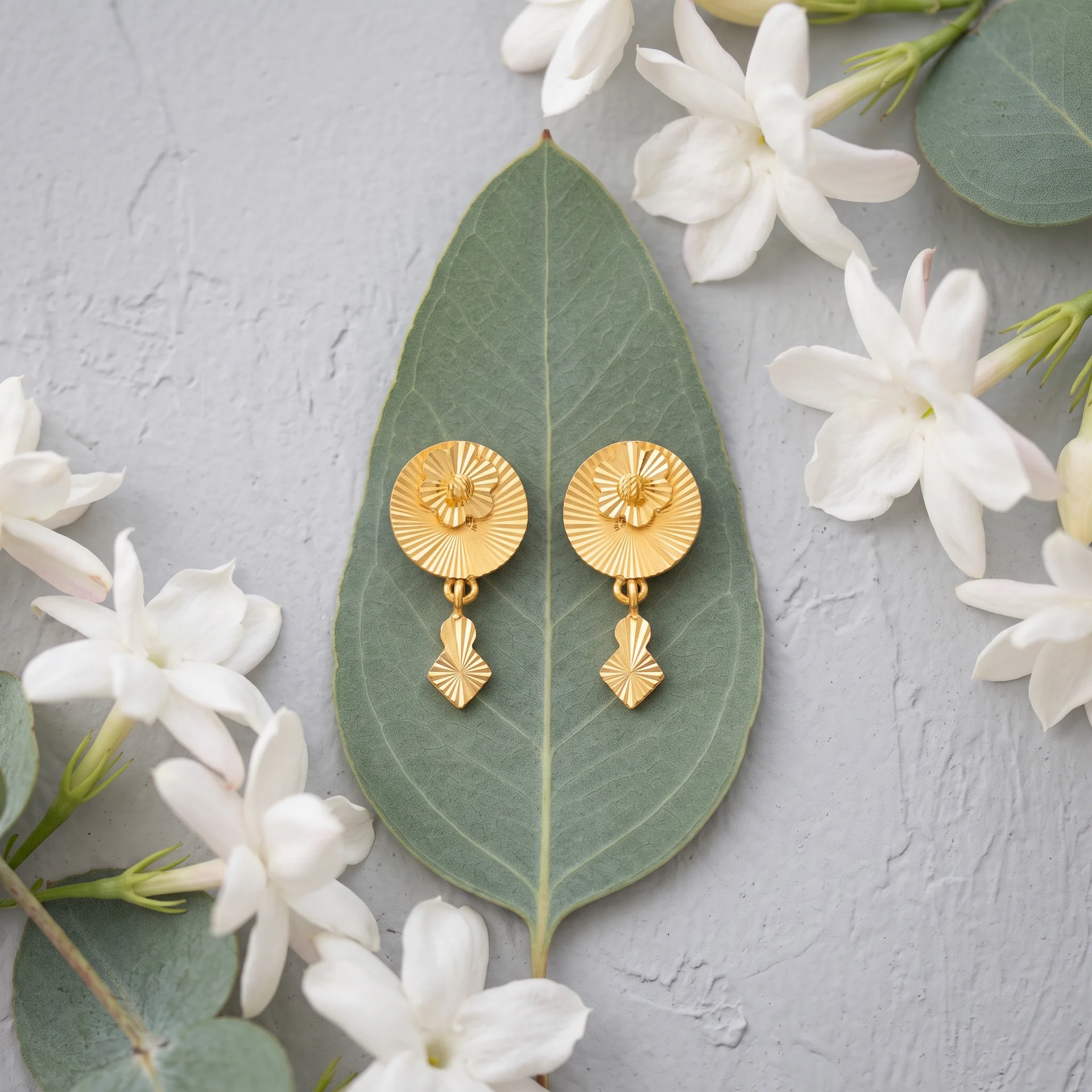 Gold drop earrings on a eucalyptus leaf with jasmine